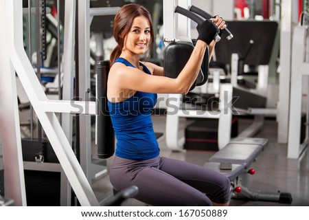 Pretty Latin young woman in a sporty outfit working out in a simulator in a gym