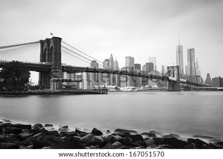 Black & White long exposure shot of the Brooklyn Bridge and New York skyline across the East River on a cloudy summer morning.