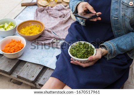 Woman hands take picture of food at home or cafe with smartphone. Phone photo of green basil walnuts pesto paste for blogging or social media. Vegan and vegetarian healthy diet.
