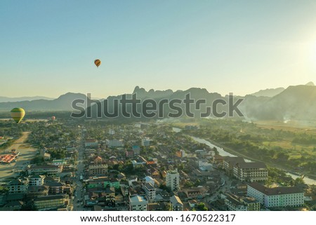Drone picture of vang vieng, laos, with air balloons, a river on the right side, some mountains and the sky in the background