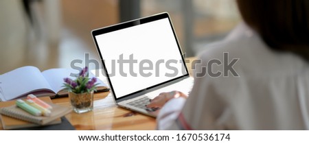 Cropped shot of  young woman university student typing on blank screen laptop with notebook and stationery on wooden counter bar