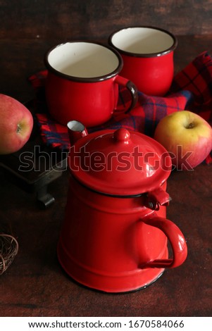 enameled red coffee pot and two mugs on a dark background