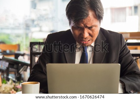Close up portrait serious middle age Asian businessman using a laptop with coffee cup at side at modern office.