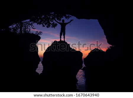 Man standing with a camera in front of a limestone cave by the sea at sunset, Photographer in front of the cave