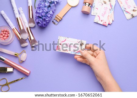 Female hand with business card of makeup artist on color background