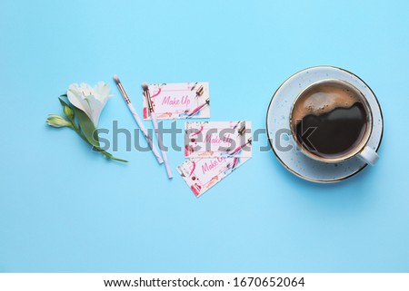 Business cards of makeup artist and cup of coffee on color background