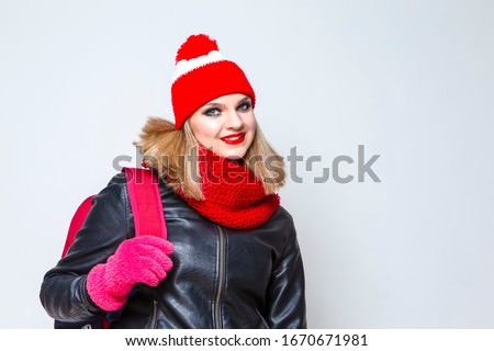 Portrait of Caucasian Blond Girl In Warm Hat and Scarf Posing in Jacket With Backpack Against White. Horizontal Image Composition