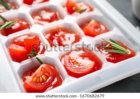 Ice cube tray with tomatoes, sauce and fresh rosemary, closeup
