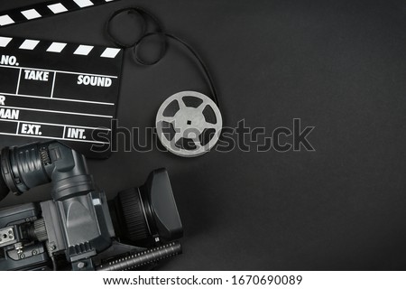 Modern video camera, movie clapper and reel on black background, flat lay. Space for text
