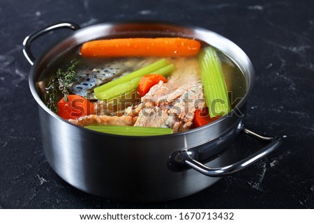 slow-cooked fish broth or soup of salmon, onion, carrot, celery, herbs and spices in a stockpot on a concrete table, horizontal view from above, close-up