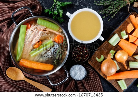 fish broth or soup of salmon, onion, carrot, celery, herbs and spices in a stockpot and in a white bowl on a concrete table with ingredients, free space, horizontal view from above, flat lay, close-up