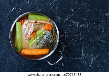 freshly cooked fish broth of salmon, onion, carrots, celery stick and spices in a stockpot on a concrete table, free space, horizontal view from above, flat lay