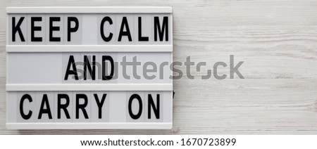 'Keep calm and carry on' words on a lightbox on a white wooden background, top view. Overhead, from above, flat lay. Copy space.