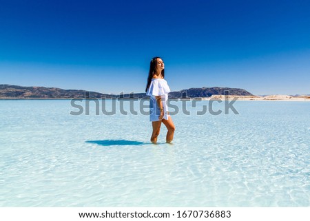Young girl in a white dress posing against the backdrop of Lake Salda and the blue sky.