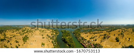 Panoramic view of a river in four thousand islands, laos, with a island in the middle, houses on the shore and rice fields all around