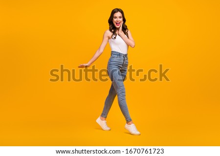 Full body profile photo of attractive cheerful lady good mood walk street arm on cheek wear white tank-top jeans footwear isolated bright yellow color background