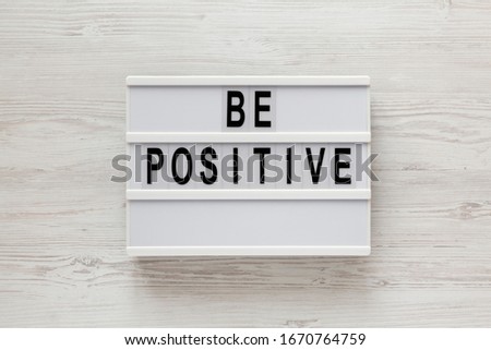 'Be positive' words on a lightbox on a white wooden background, top view. Overhead, from above, flat lay. 