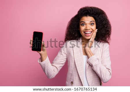 Photo of beautiful shocked dark skin lady hold telephone hand on cheek presenting new smart phone model sale price wear checkered blazer isolated pastel color background