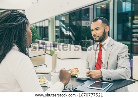 Multiethnic business colleagues discussing project over cup of coffee. Business man and woman sitting at table in cafe, drinking coffee and talking. Corporate communication concept