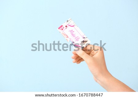 Female hand with business card of makeup artist on color background