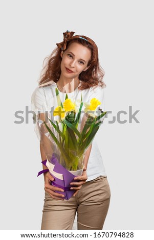 Caucasian attractive girl with a smile on her face extends to the viewer a bouquet of narcissists. Woman has tan skin and a slender figure. White background