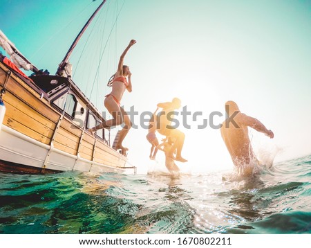 Happy friends diving from sailing boat into the sea - Young people jumping inside ocean in summer excursion day - Vacation, youth and fun concept - Main focus on close-up man - Fisheye lens distortion Royalty-Free Stock Photo #1670802211