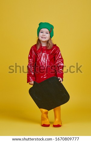 Little child girl holding black chalkboard banner on yellow background. Funny Face. Copy space for text. Advertising seasonal childrens products