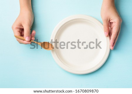 Hand holding biodegradable plate, Compostable plate or Eco friendly disposable plate and wooden spoon on pastel color background, Top view