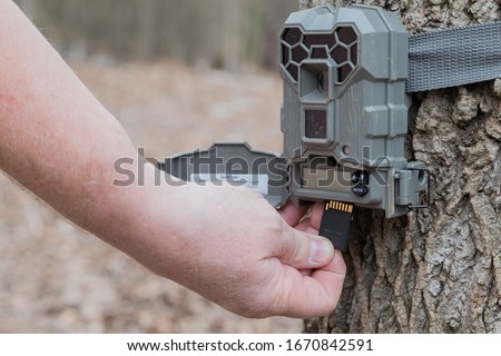 A man taking the SD card out of a motion activated trail camera to check the photos for wild game. Trail cameras are often used by hunters and wildlife enthusiasts to survey the animals in the area.