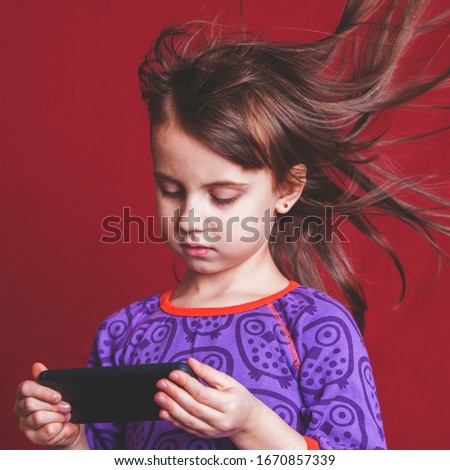 Psychological image of cute little girl addicted to likes: Social networks feeds her neediness. Portrait of nervous child with mobile smart phone. Negative emotion and emotional addiction concept. 
