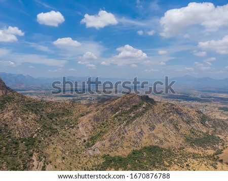 drone shot aerial view mountains hills peaks shadows dry cliffs blue sky bright sunny day beautiful weather white clouds rugged terrain tamilnadu india top angle scenic background wallpaper 