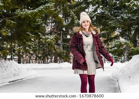 Smiling woman in warm clothes  having a great time ice skating in snowy winter park. Winter holidays concept