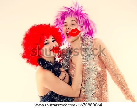 Attractive playful young women ready for carnival parties. Lifestyle and the concept of friendship: a group of two girl friends. Isolated on gray. Paper lips on a stick