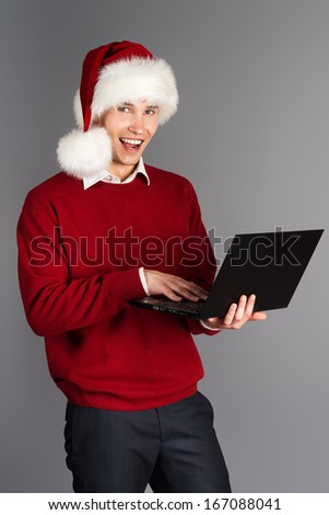 Young businessman in Santa Claus cap standing with a laptop.