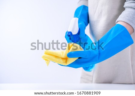 Young woman housekeeper is doing cleaning white table in apron with blue gloves, spray cleaner, wet yellow rag, close up, copy space, blank design concept.