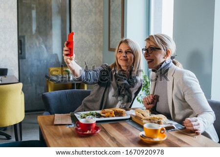 women friends having lunch break in restaurant , using mobile device fro taking picture