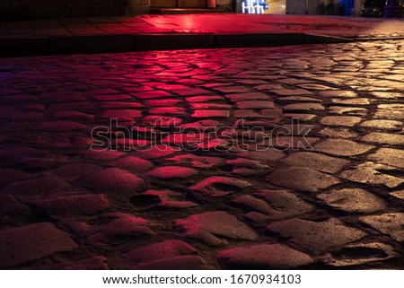 Wet illuminated by red light cobblestone street at night