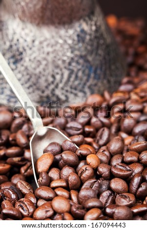 spoon scoops roasted coffee beans and copper coffee pot close up