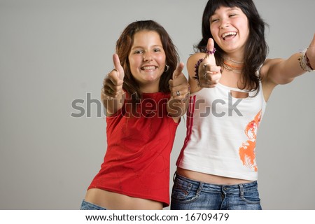 A studio view of two happy teenage girls reaching out with open arms and smiling happily.