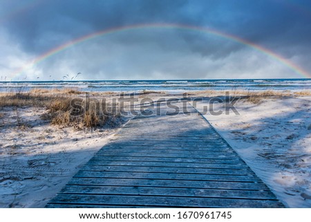 Rainbow and Wooden Walkway at a Baltic Sea Beach with Waves in the Winter Royalty-Free Stock Photo #1670961745