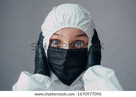 Virologist in black mask in a viral protective suit holds head, looks at the camera with fear and thinking about how to stop the coronavirus epidemic and what to do. Thinks about the dangers of this. Royalty-Free Stock Photo #1670977096