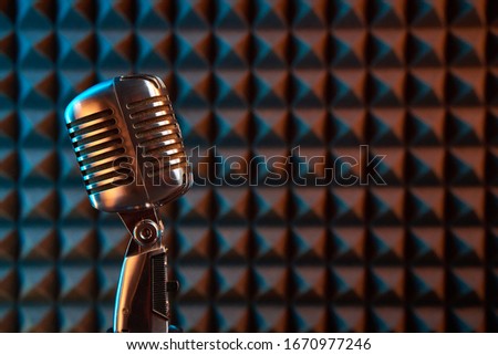 Retro microphone on acoustic foam panel background, colorful light, closeup