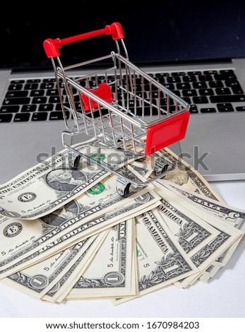 Online shopping concept image with a miniature shopping cart and cash on a laptop.