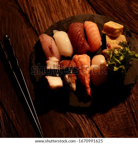 Dark mood photography set of sushi with chopstick, served on black stone plate on wooden table background. Eye level angle concept. 