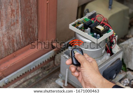 Technician man hand using remote control, testing and checking the functional of auto door. Maintenance and repairing automatic gate concept.  