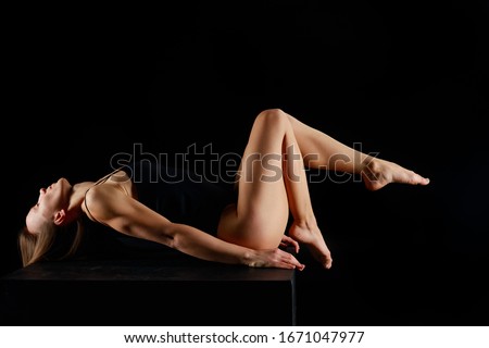 woman in bodysuit lying while practicing yoga isolated on black