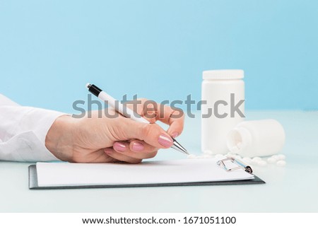 doctor’s hands in a white medical coat push the pen on the prescription, two white jars with pills  on a blue background. concept of medicine, cardiology