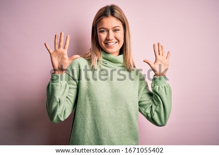 Young beautiful blonde woman wearing winter wool sweater over pink isolated background showing and pointing up with fingers number ten while smiling confident and happy.