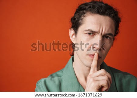 Image of displeased caucasian man gesturing silence sign at camera isolated over orange background