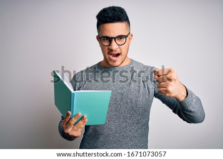 Young handsome smart student man reading book over isolated white background annoyed and frustrated shouting with anger, crazy and yelling with raised hand, anger concept